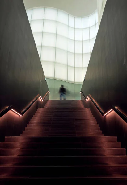 man walking up stairs into the light in a modern and futuristic architecture