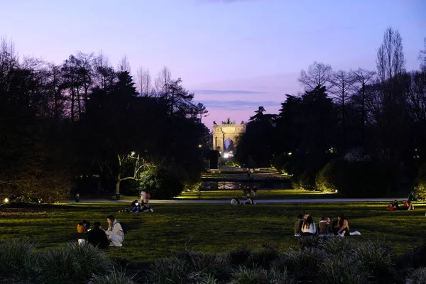 Milano 'daki Sempione Parkı ve Barış Kemeri' nde geceleyin oturan insanlar - ITA - 2023 Mart