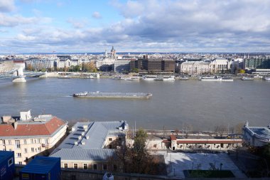 Budapeşte 'de Tuna Nehri' nde yüzen bir kargo gemisi: tarihi nehir boyunca ticaret ve bağlantıyı sembolize eden şehir manzarasına karşı endüstriyel bir gösteri