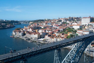 Porto 'nun panoramik manzarası, nehir, ikonik köprü ve tarihi eski kasaba. Şehrin zengin tarihini ve hareketli atmosferini gözler önüne seren çarpıcı bir manzara..