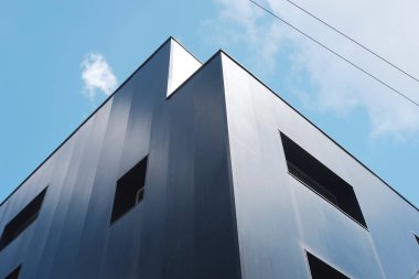 Keskin kenarlı siyah modern bina. Minimum pencereli. Parlak mavi gökyüzü ve dağınık bulutlar.