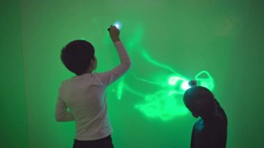 Bilim ve fizik, meraklı erkek çocuklar el fenerleriyle oynayıp duvarlara yeşil odada ışık saçan desenler çizerek eğleniyorlar.