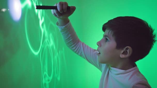 賢い男性の子供は科学や物理学に興味があり紫外線で緑の壁に絵を描いています — ストック動画