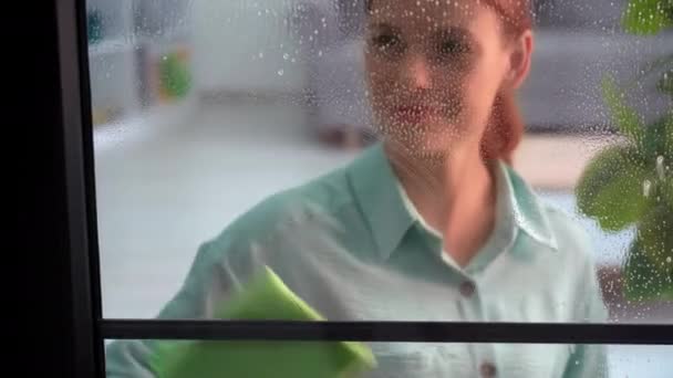 一个戴手套的年轻快乐女人的肖像用清洁剂和餐巾擦窗户 微笑着看着相机 — 图库视频影像