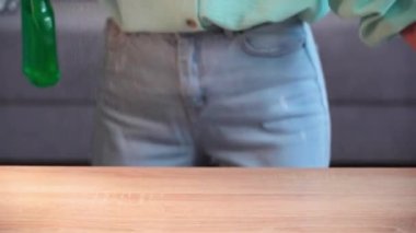 Apartman temizliği, eldivenli kadın mikrofiber bez kullanıyor ve sprey şişedeki deterjan masayı toz ve pislikten temizliyor, yakın plan.