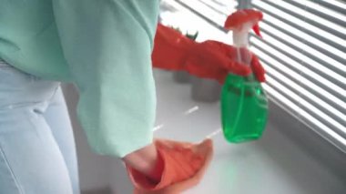 Prezervatif ve mikrofiber bez kullanan koruyucu mühürlü bir kadın evi temizlerken jaluzileri ve pencere perdelerini yıkıyor.