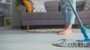 room cleanliness, hardworking woman uses a mop and washes laminate in home background of furniture, close-up
