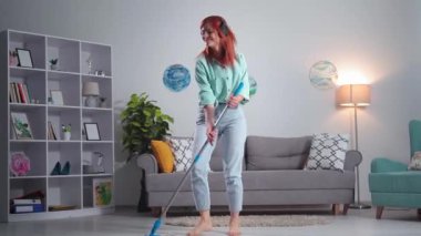 cheerful cleaning, happy young woman with a mop in hands listens to music on headphones, sings and washes the floor in apartment