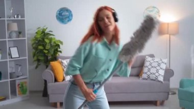 beautiful young woman in headphones dancing with mop in hands during cleaning at home