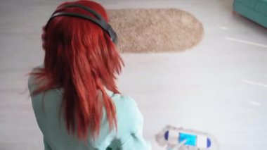 cheerful cleaning, young woman in headphones dancing with a mop while cleaning house, top view