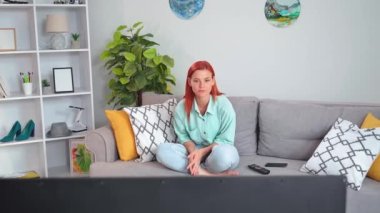 good news, young woman watching news on tv and making phone calls to friends while sitting on sofa in room