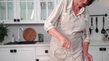Yaşlı kadın emekliler düzgün bir hayat sürüyorlar ve şeffaf bir bardakta temiz su içiyorlar. Mutfakta durmuş gülümsüyor ve kameraya bakıyorlar.