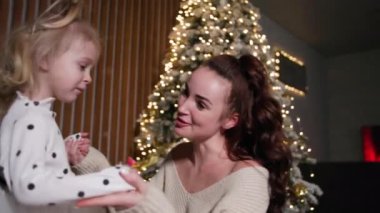 family fun, female parent having fun together with their daughter playing and dancing near the Christmas tree in the late evening at home