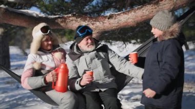 relationship of children and parents, happy boy together with grandparents drink hot tea while sitting in hammock during joint walk in forest