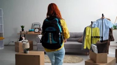 homecoming, happy woman takes off backpack and sits on sofa, smiles and looks at camera