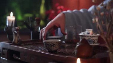 young woman takes bowl with hot drink while holding a tea ceremony while sitting at table indoors, close-up