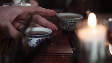tea ceremony, womans hand takes a hot drink in a bowl background of a hot candle, close-up