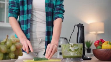 Modern diyet menüsü, genç ince kadın doğru beslenmeyi izler ve mutfak masasındaki blender içinde taze sebzelerden vejetaryen smoothie hazırlar.