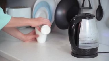 Kahve molası, kadın mutfakta kahve yapmak için elektrikli su ısıtıcısının kaynamasını bekliyor.