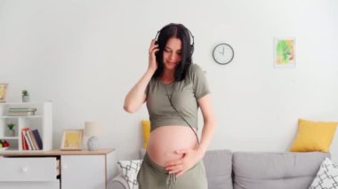 happy pregnant woman listening to music with headphones for good mood in the room