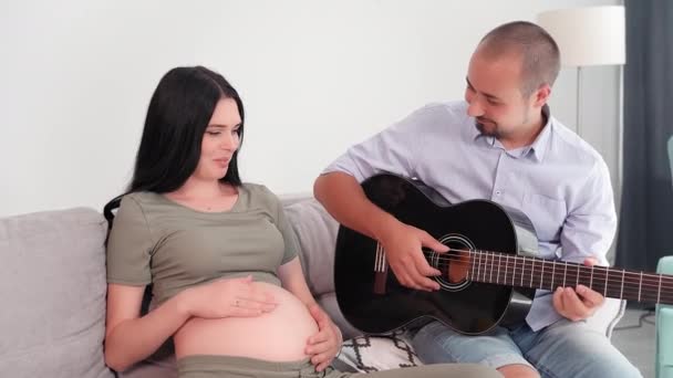 Paternidad Padre Feliz Toca Guitarra Para Esposa Embarazada Sentada Sofá — Vídeos de Stock