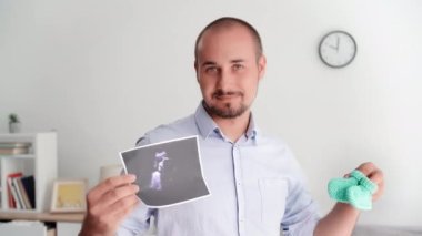 portrait of young man with booties and photograph of an ultrasound in hands expecting baby smiling and looking at camera