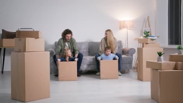 幸せな家族は新しいアパートを購入することを喜びます 思いやりのある若い両親は 新しい家に移動しながら 床に箱に自分の子供を転がす楽しみを持っています — ストック動画