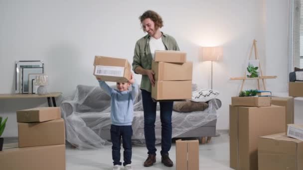家族の夢幸せな若い父親と息子の手に箱がある新しい家に引っ越し住宅ローンを支払うことを喜ぶ家具付きソファの背景 — ストック動画