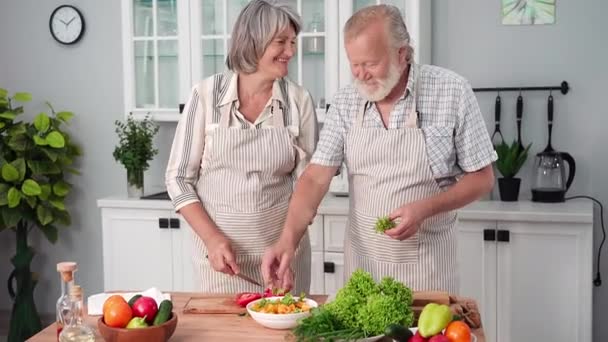 退休男女穿着围裙 用厨房里摆在桌旁的新鲜成熟蔬菜一起准备午餐 — 图库视频影像