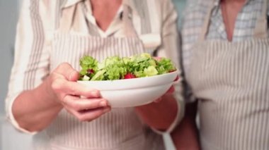 Yaşlı bir çiftin portresi sağlıklı bir hayat sürüyor ve diyet izliyor, elinde atıştırmalık taze sebze salatası tutuyor, gülümsüyor ve kameraya bakıyor