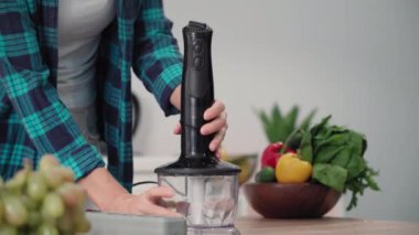 Ev eşyaları, genç bir kadın yemek pişirmek için blender takıyor, yakın plan.