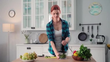 Genç bir ev kadınının portresi doğru beslenmeyi gözlemliyor ve mutfakta durup gülümseyen ve kameraya bakan, sınıfını gösteren bir blender içinde sebze ve marul yaprakları öğütüyor