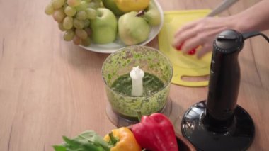 Genç bir kadın biberi keser ve öğütmek ve mutfak masasında smoothie yapmak için miksere atar.