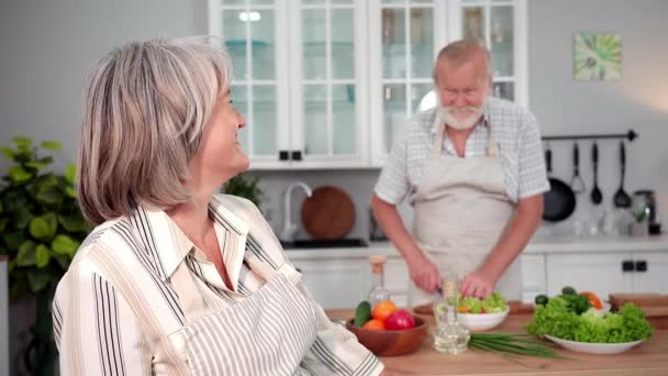 낭만적 식사를 부엌에서 샐러드를 자르는 남편의 앞치마를 즐거운 노부인의 미소짓고 — 비디오