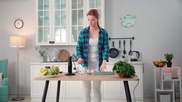家用电器 年轻漂亮的女人站在厨房的桌子旁边 把搅拌机插在插座上 用来制造光滑的东西 — 图库视频影像