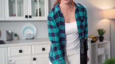 Elinde bir bardak taze yeşil smoothie tutan, gülümseyen ve arka plandaki kameraya bakan çekici bir genç kadının portresi.