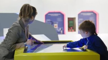 Çocuklar için öğrenme teknolojileri, sevimli bir kadın ve küçük zeki bir çocuk kapalı alanda elektronik harita çalışırken parmaklarını dokunmatik ekranda gezdiriyorlar.