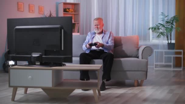 Дедушка Использует Играть Видеоигры Телевизоре Помощью Беспроводной Игровой Консоли Сидя — стоковое видео