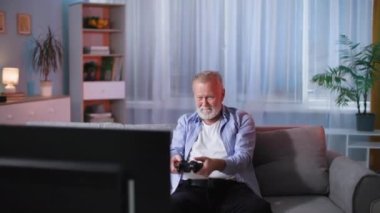 Oyuncu, yaşlı adam evdeyken televizyon karşısında kanepede otururken konsolda video oyunu oynuyor.