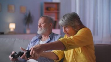 Emeklilikte eğlence, yaşlı aile TV 'de oyun kağıtlarıyla neşe içinde video oyunları oynuyor, yaşlı kadın akşamları koltukta otururken oyunu kazanmaktan duygusal olarak zevk alıyor.