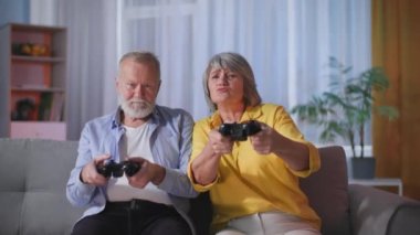 Yaşlı karı ve koca, akşamları evde boş vakitlerinde kanepede televizyon karşısında otururken joystickler ve konsollar kullanarak video oyunları oynayarak eğleniyorlar.