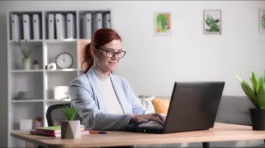 Uzaktan çalışma, gözlüklü gülümseyen kadın bilgisayar ekranına bakar, masadaki klavyede daktilo yazar.
