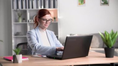 Gözlüklü sevimli bayan çalışan ofiste bir masada otururken bilgisayarın başında klavyeyle yazı yazıyor.