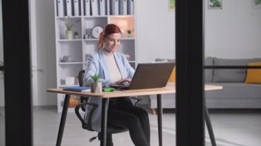 Evde çalışıyor, gözlüklü güzel bayan yönetici odada bilgisayar başında çalışıyor, gülümsüyor ve kameraya bakıyor.