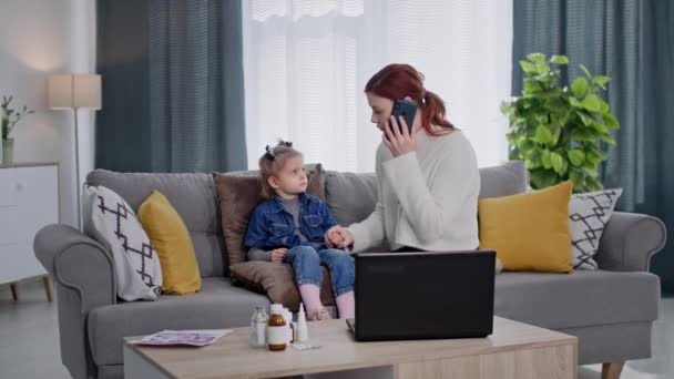 若い母親はモバイル接続で医師と話しています部屋のソファに座っている少女のための薬の選択について相談しています — ストック動画