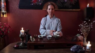 Profesyonel kadın çay ustası çay seremonisi yapar ve masada otururken sıcak suyu kaselere döker.