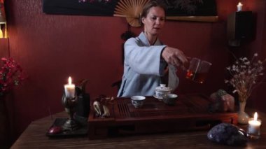 Çay seremonisi yapan ve Buddha ve ejderha heykelciklerinin üzerine sıcak çay döken teamaster masada otantik çay eşyasıyla oturuyor.