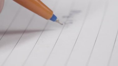 Elinde kalem olan kadın masada otururken not defterine not alıyor, yakın plan.