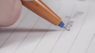 Tükenmez kalem deftere notlar yazar. Masaya yakın plan.