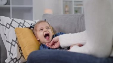 Çocuk sağlığı, küçük bir kız yastığa uzanır ve ağzını açar. Annesine odada kanepede yatarken boğazını gösterir.